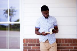 male-leaning-against-wall-while-reading-bible