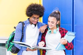 diverse-teenage-couple-standing-against-blue-yellow-wall-studying-together